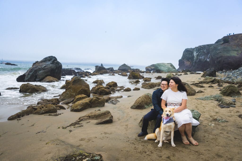 Couple with their dog enjoying a beach photoshoot, captured in a natural and candid moment by a San Francisco Bay Area wedding photographer.